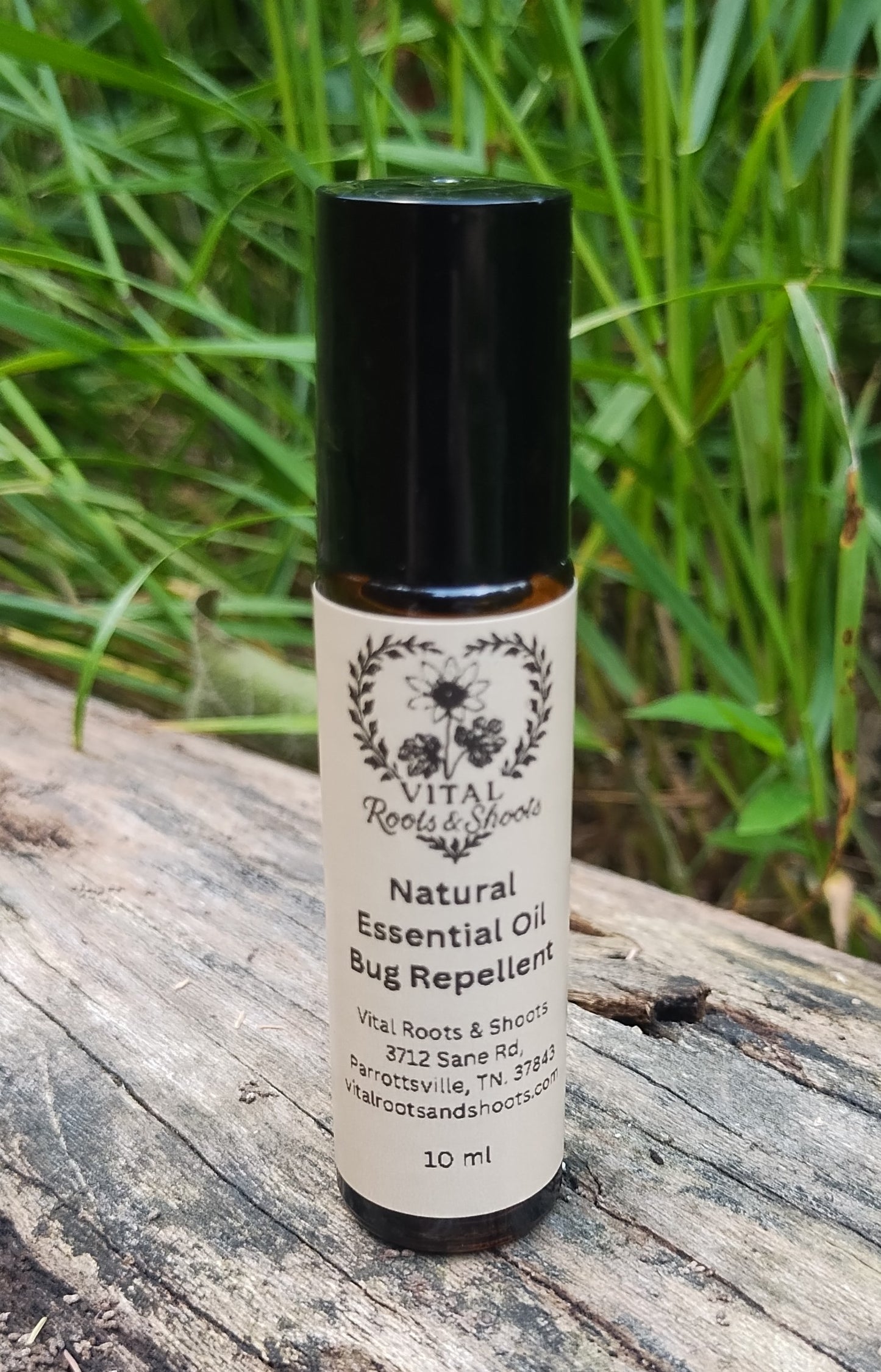 Natural herbal bug repellant in an aromatherapy roller bottle on a log with grass and plants in the background.