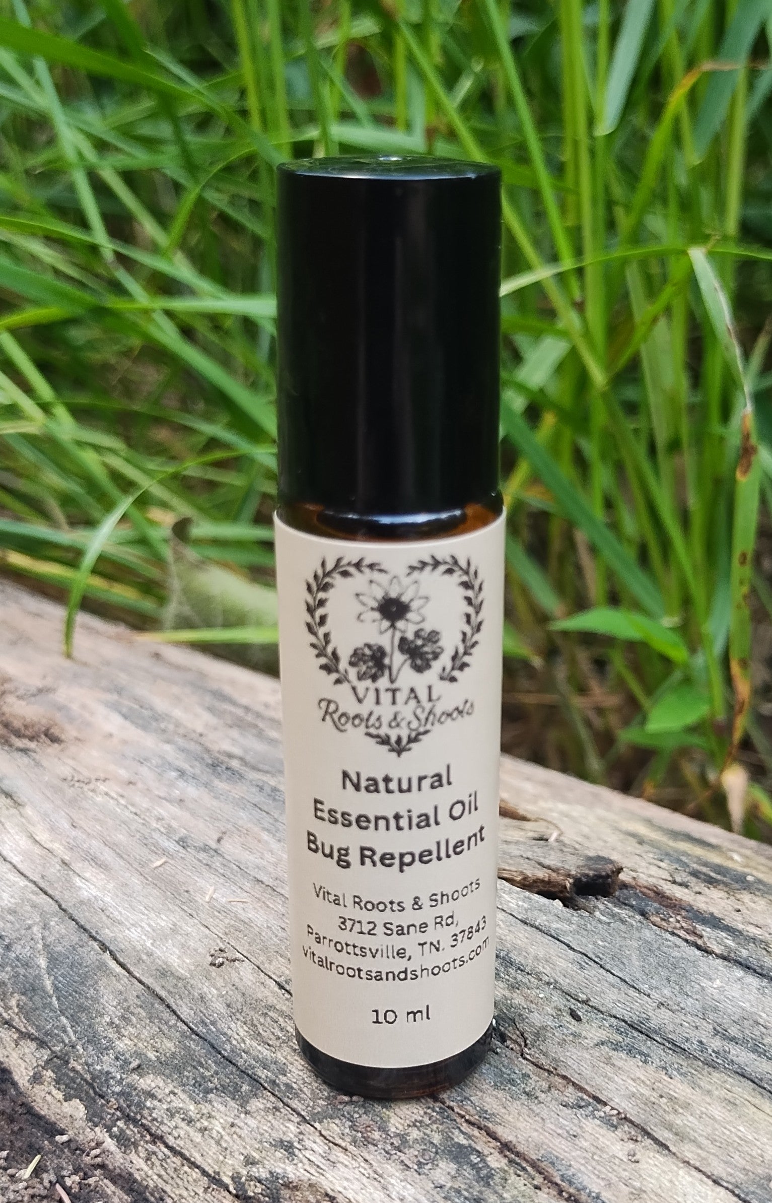 Natural herbal bug repellant in an aromatherapy roller bottle on a log with grass and plants in the background.