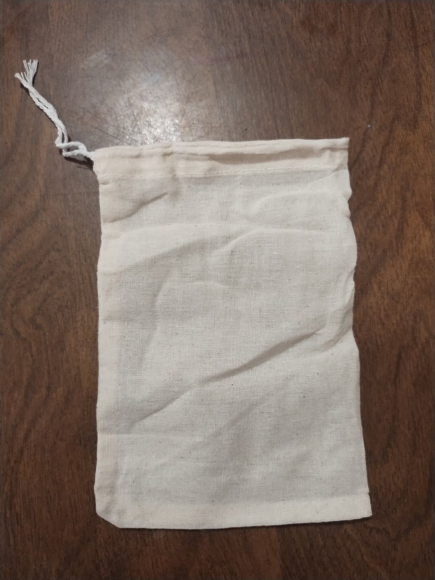 A reusable unbleached cotton bag with drawstring four inches wide by six inches long.